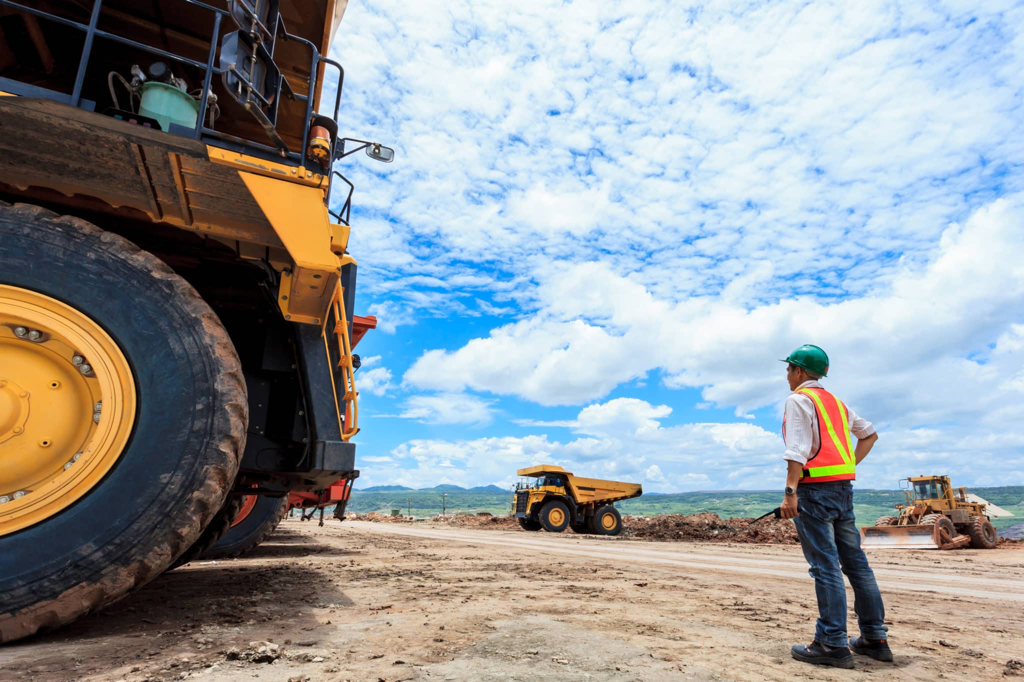 A site worker stood next to a huge earthmover wheel, onsite with trucks in the background.